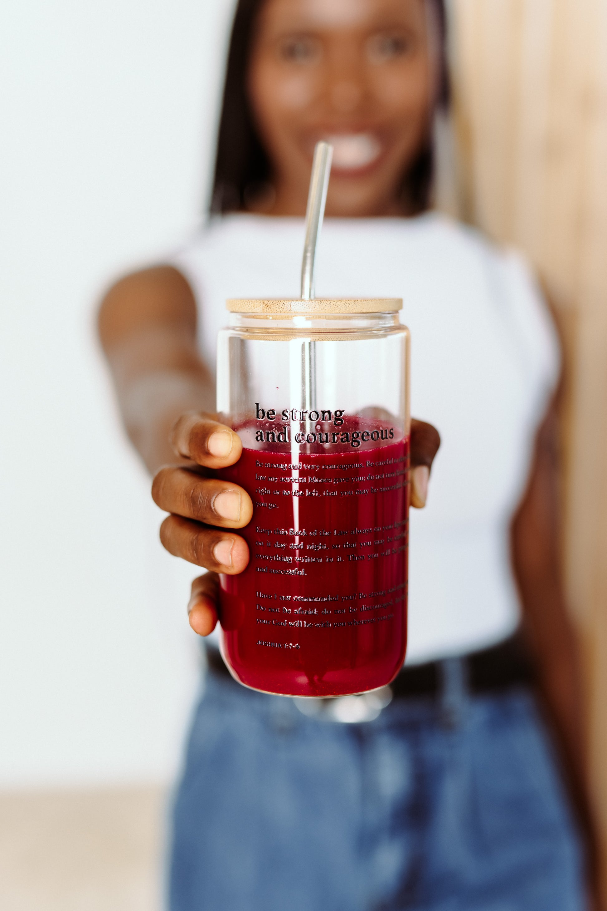 Person holding a clear tumbler be strong and courageous  with red liquid and a straw, blurred background