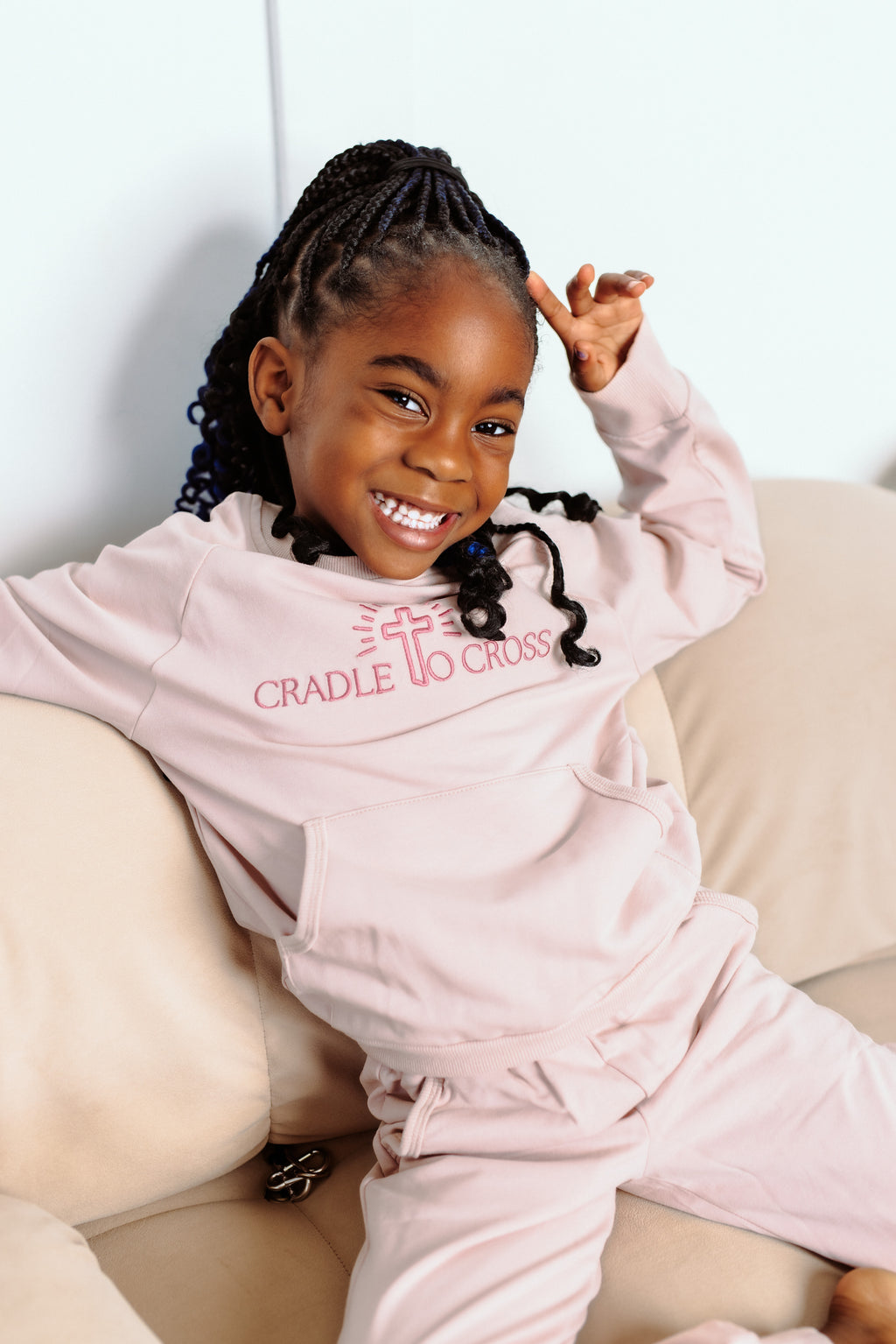 Child wearing a pink 'Cradle to Cross' outfit sitting on a couch.