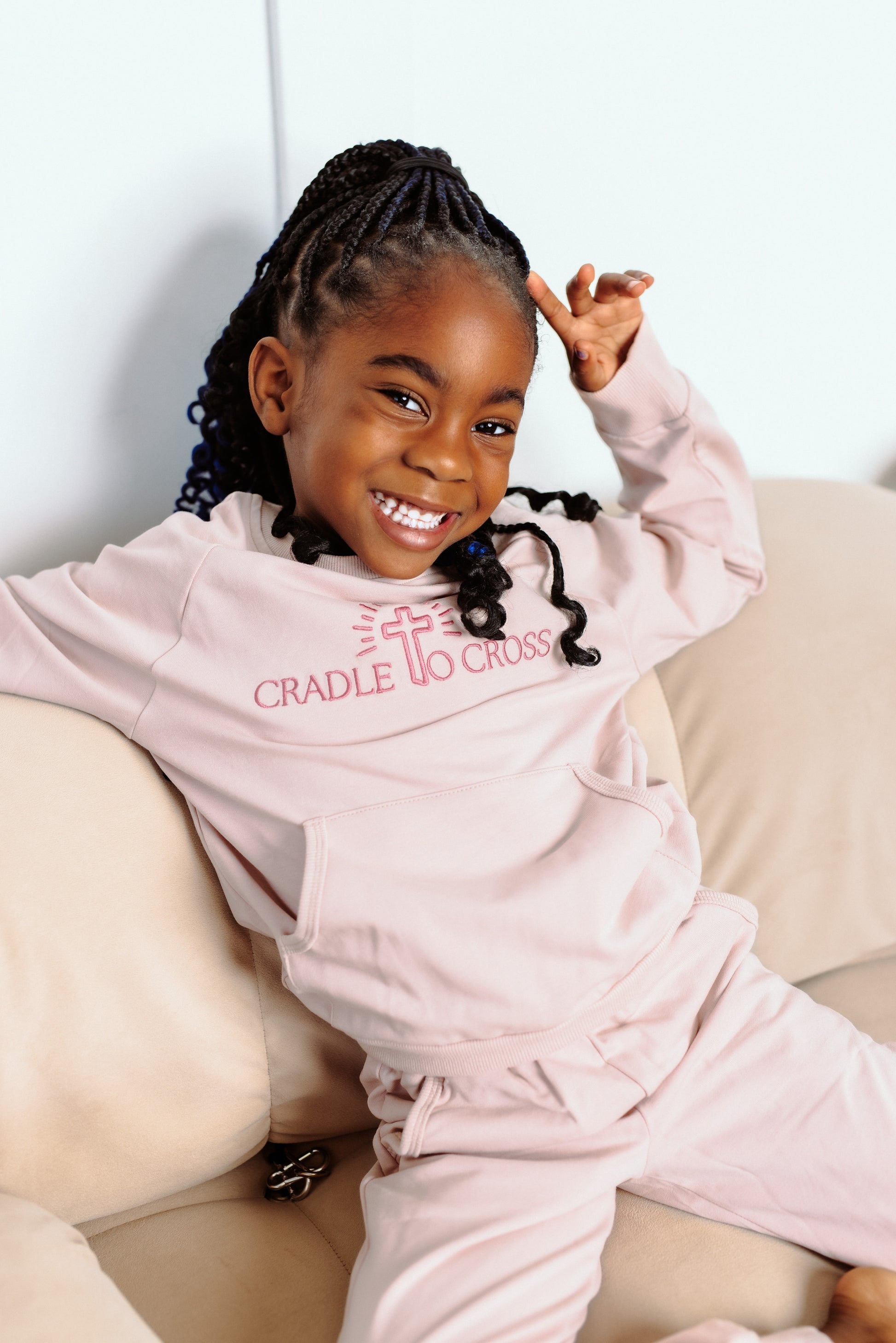 Child wearing a pink 'Cradle to Cross' outfit sitting on a couch.