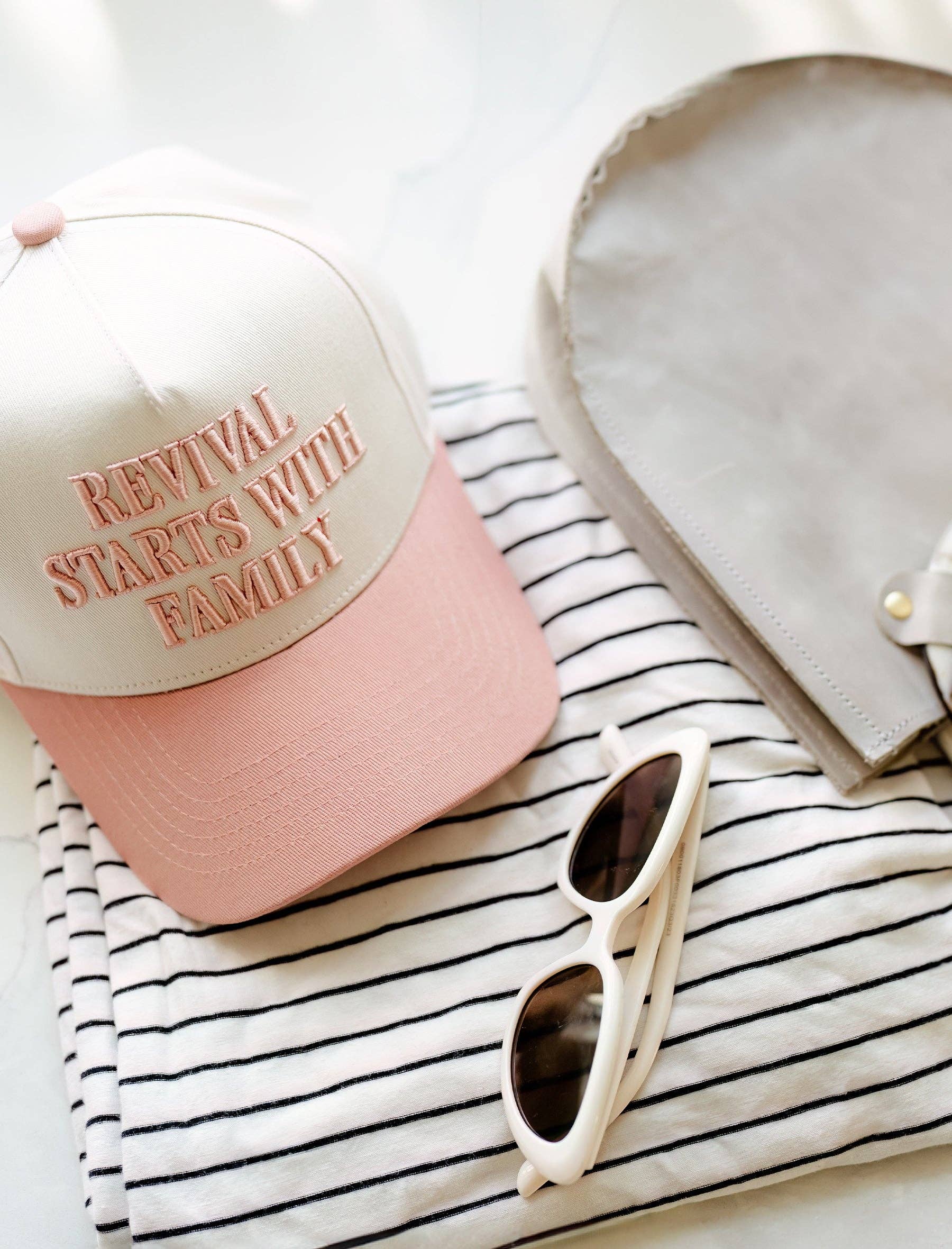 Pink cap with text, sunglasses, and heart-shaped object on striped fabric